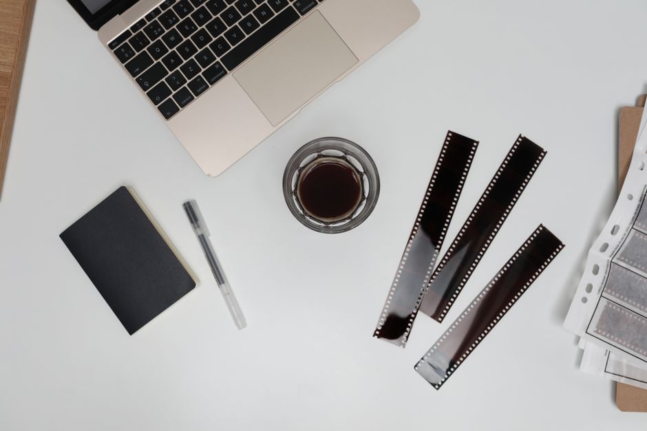 Top view of filmstrips with coffee cup and notebook placed on working desk with opened laptop